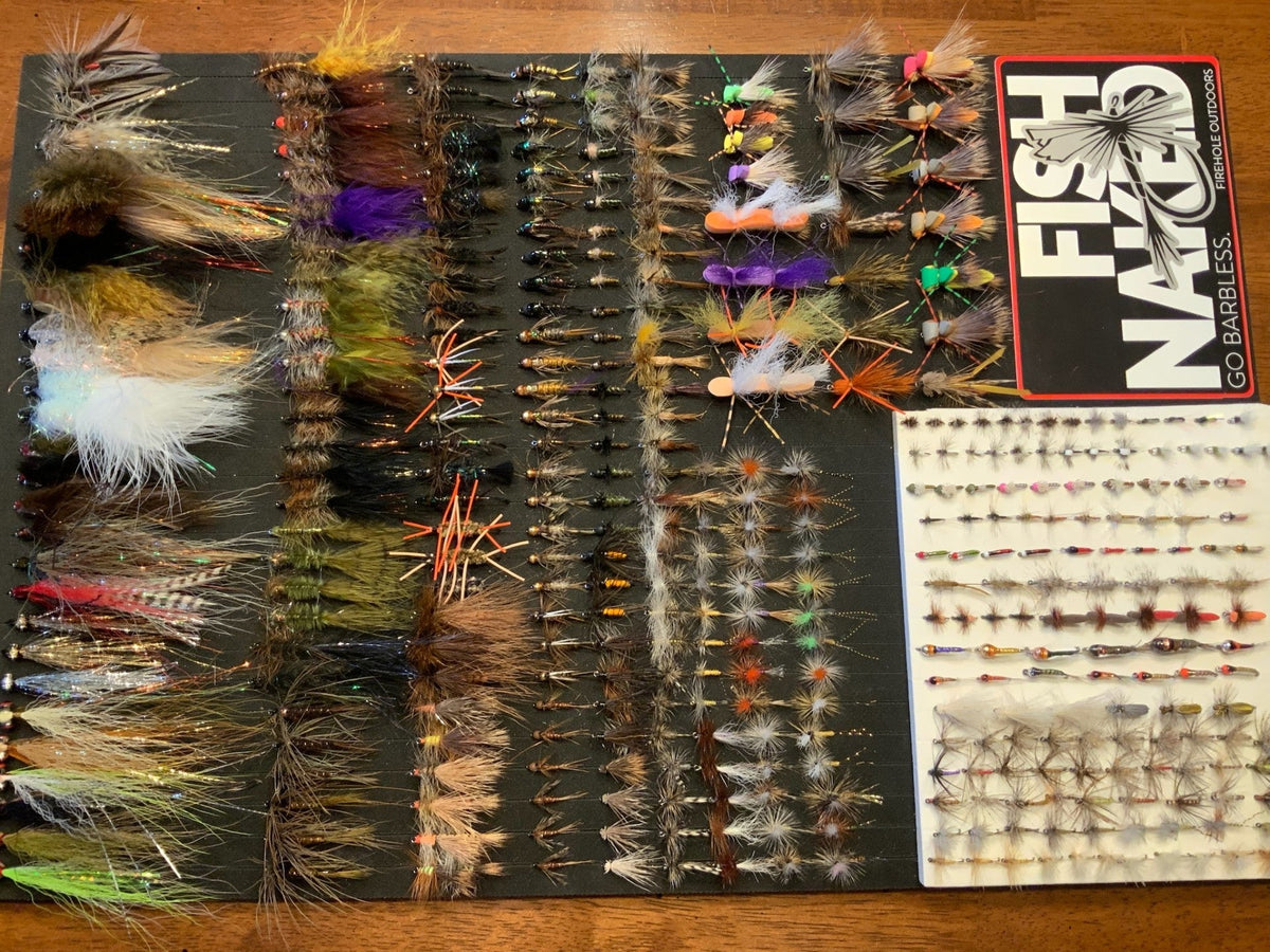Rows of hand-tied streamers, nymphs and dry flies laid out on a foam board beside a Firehole Outdoors Go Barbless sticker
