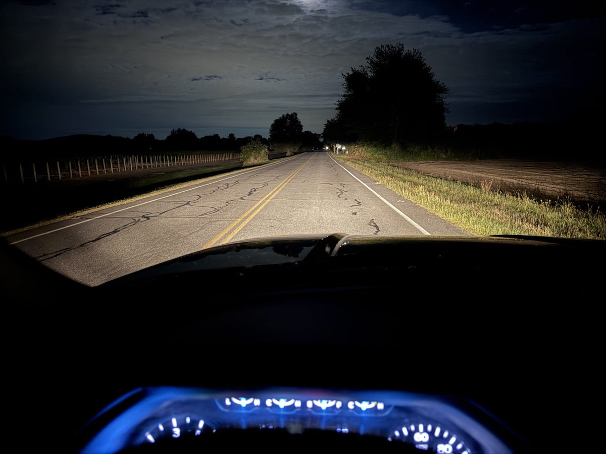 Headlights on a dark two-lane road seen through a truck windshield, with the instrument cluster glowing at the bottom of the frame